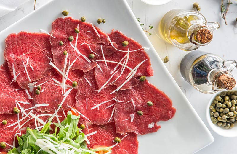 Plato de carpaccio de carne roja con ensalada.