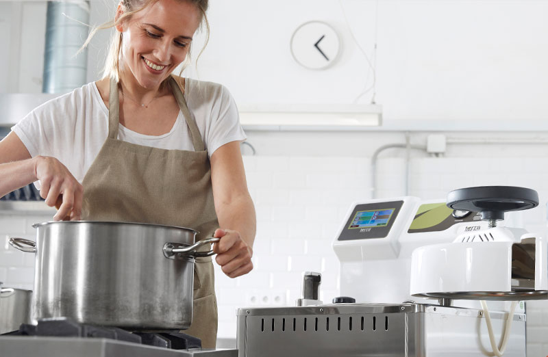 Preparación de alimentos para la esterilización de carne en conserva. En la imagen se muestra una mujer cocinando al lado de la autoclave vertical CFS-V de TERRA Food-Tech.